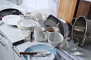 Many dirty utensils and dishware on countertop in messy kitchen