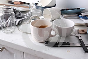 Many dirty utensils and dishware on countertop in messy kitchen