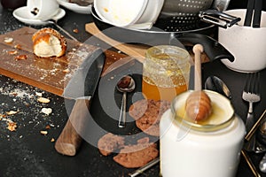 Many dirty utensils, dishware and food leftovers on black countertop. Mess in kitchen