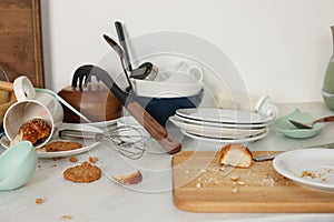 Many dirty utensils, dishware and food leftovers on white countertop. Mess in kitchen