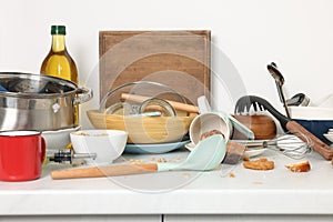 Many dirty utensils, dishware and food leftovers on white countertop. Mess in kitchen