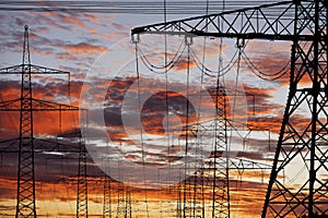 Many elecrtic poles in front of sky with clouds