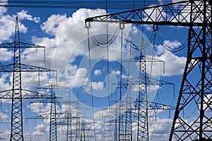 Many electric poles in front of sky with clouds