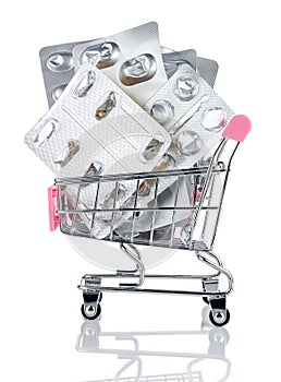 Many empty blister packs of tablets and pills in chromed toy market shopping cart with pink handle isolated on white background