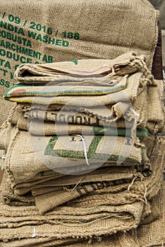 Many empty coffee beans bags folded and lying on a pile a sack hangs in the background with non-saying partial print