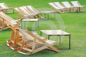 Many empty white deck chairs with tables in lawn is surrounded by shady green grass. Comfortable on outdoor patio chairs in garden
