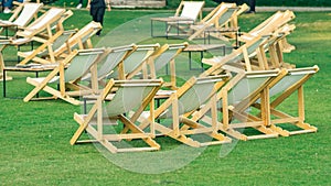 Many empty white deck chairs with tables in lawn is surrounded by shady green grass. Comfortable on outdoor patio chairs in garden