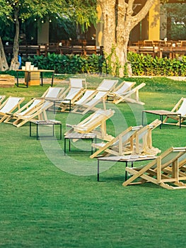 Many empty white deck chairs with tables in lawn is surrounded by shady green grass. Comfortable on outdoor patio chairs in garden