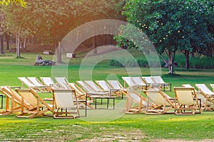 Many empty white deck chairs with tables in lawn is surrounded by shady green grass. Comfortable on outdoor patio chairs in garden