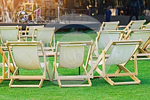 Many empty white deck chairs with tables in lawn is surrounded by shady green grass. Comfortable on outdoor patio chairs in garden