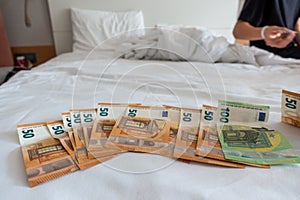 Many euro banknotes are spread out on a bed with a white duvet cover