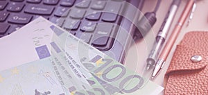 Many 100 euros lie on the laptop keyboard, two pens and leasther wallet besides. Online business internet shop web project concept photo