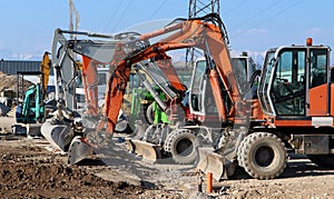 Many excavators of different colors and sizes lined up at the construction site, waiting to get back to work