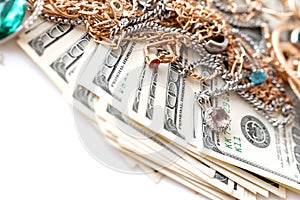 Many expensive golden and silver jewerly rings, earrings and necklaces with big amount of US dollar bills on white background.