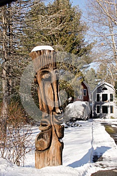 Faces of a totem pole in the direct sunlight with snow atop