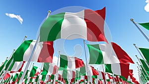 Many flags of Italy on flagpoles against blue sky.