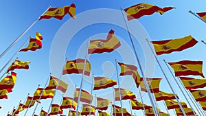 Many flags of Spain waving against blue sky.