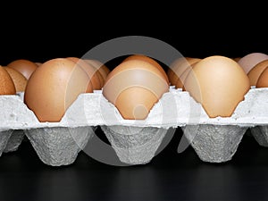 Many fresh brown eggs on paper tray on black background