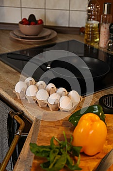 Many fresh eggs in carton and bell pepper on wooden countertop in kitchen. Ingredients for breakfast