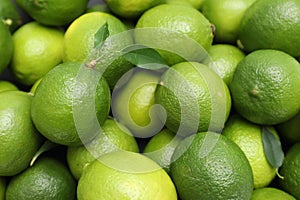 Many fresh limes with green leaves as background, top view