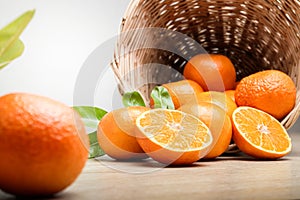 Many fresh oranges in a wooden basket placed on the floor. There are some balls that have been cut in half to make them look appet