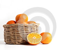 Many fresh oranges in a wooden basket placed on the floor. There are some balls that are cut in half to make them look appetizing.