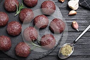 Many fresh raw meatballs and ingredients on black wooden table, flat lay