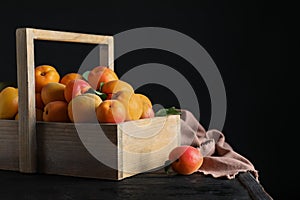 Many fresh ripe apricots in wooden basket on table against black background. Space for text