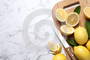 Many fresh ripe lemons with green leaves and knife on white marble table, flat lay. Space for text