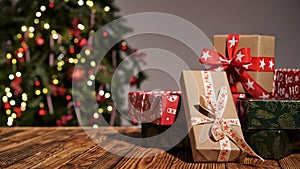 Many gift boxes wrapped in multi-colored paper on a wooden table against the background of a beautiful Christmas tree, copy space