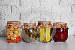 Many glass jars with different preserved vegetables and mushrooms on light grey table