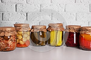 Many glass jars with different preserved vegetables and mushrooms on light grey table