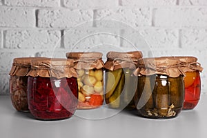Many glass jars with different preserved vegetables and mushrooms on light grey table