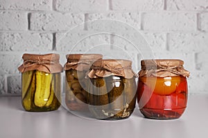 Many glass jars with different preserved vegetables and mushrooms on light grey table