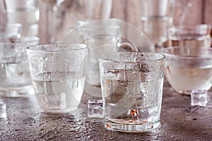 Many glasses of water splashed with drops and pieces of ice