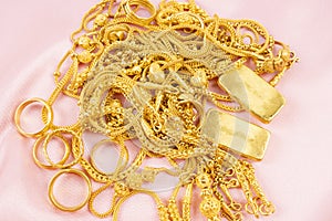 Many gold necklaces and gold bars on pink cloth background