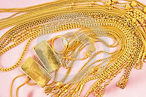 Many gold necklaces and gold bars on pink velvet cloth
