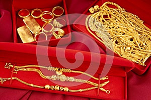 The Many gold necklaces and gold bars in red box on red velvet cloth background