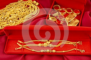The Many gold necklaces and gold bars in red box on red velvet cloth background