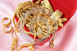 Many gold necklaces and gold bars in red box on velvet cloth