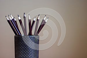 Many graphite pencils standing in black glass container.