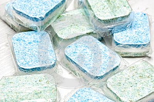 Many green and blue dishwasher tablets in water-soluble packaging close up