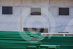 Many green metal roof structure on the floor in front of building structure in construction site