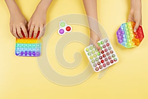 Many hands holding pop it fidget toys on yellow background. Push pop-it fidgeting game helps relieve stress, anxiety