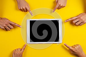 Many hands pointing to white tablet computer with blank screen on yellow background