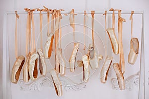 Many hanging ballet shoes on white wall background in studio. New pointe shoes with satin ribbons hanging on rank. Ballet shoes ha