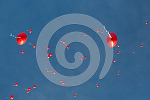 Many heart-shaped red balloons flying in blue sky