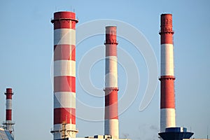 Many high red and white industrial pipes over clear cloudless blue sky on sunny day