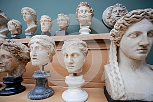 Many human faces and marble heads copies of old Roman gods and emperors on shelf. Memories about human of ancient world