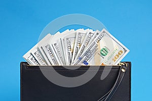 Many hundreds of dollars looks out of a black leather wallet on a blue background